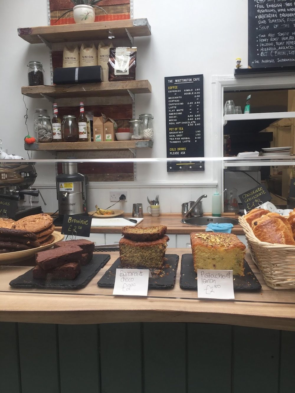 The wooden service counter with the espresso machine, shelves of jars and syrups, and cakes and pastries laid out