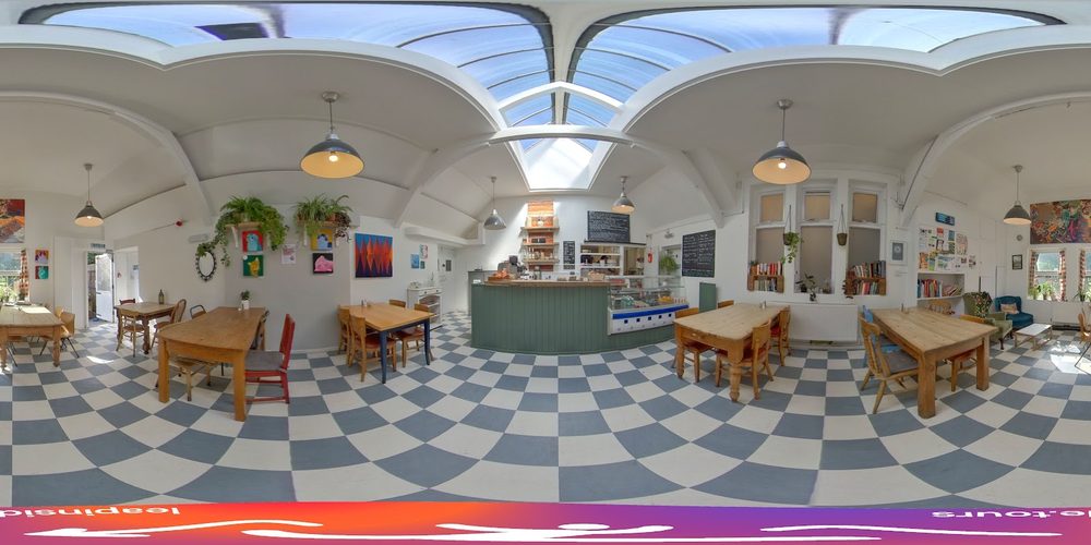 The glass-roofed cafe room at Whittington Park Community Centre, with a blue-and-white chequerboard floor, wooden tables and hanging plants
